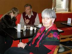 Gäste: eine Frau unterhält sich mit einem älteren Herrn, davor eine Frau in rotem Pullover mit grauem Haar.