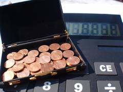 Schwarzer Koffer mit Münzen steht auf einem riesigen Taschenrechner