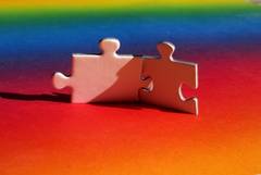 Zwei ineinander verhackte Puzzleteile vor einem Hintergrund in Regenbogenfarben