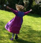 Mädchen mit violettem Kleid tanzt auf Wiese.