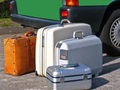 Vier Koffer stehen - fertig für die Reise - vor dem Kofferraum eines grünen Fahrzeugs