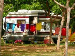 Wohnmobil unter Bäumen, bunte Wäsche davor aufghängt