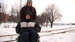junger Rollstuhlfahrer mit Assistenten in verschneiter Landschaft
