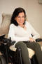 Portrait einer lächelnden Frau mit dunklen Haaren und weißem Pullover im Rollstuhl