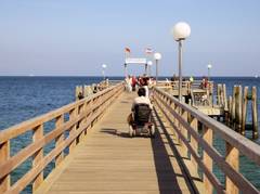 Frau im Rollstuhl steht am Pier und schaut auf das Meer hinaus