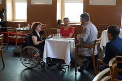Ein Moderator mit Headset spricht mit zwei Frauen an einem Tisch in einem Cafe mit Studio