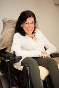 Portrait einer lächelnden Frau mit dunklen Haaren und weißem Pullover im Rollstuhl