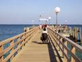 Frau im Rollstuhl steht am Pier und schaut auf das Meer hinaus