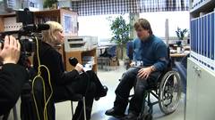 eine blonde junge Frau interviewt einen jungen Mann im Rollstuhl