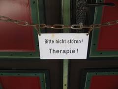 Eine alte, große Tür; vor der Tür hängt ein Schild mit "Bitte nicht stören! Therapie" 